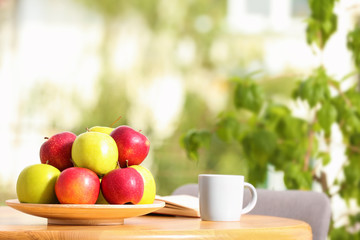 Plate with different sweet apples and cup of coffee on table in room