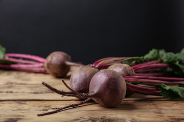 Fresh beets with leaves on wooden table against black background. Space for text
