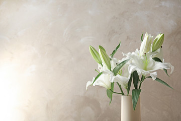Vase with beautiful lilies on light brown background, space for text