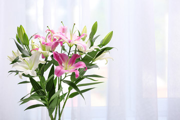 Vase with bouquet of beautiful lilies on blurred background. Space for text
