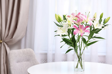 Vase with bouquet of beautiful lilies on white table indoors. Space for text
