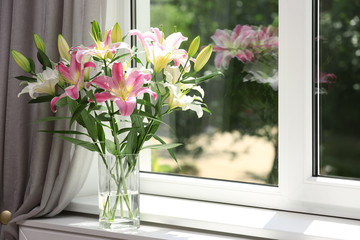 Vase with bouquet of beautiful lilies near window indoors. Space for text