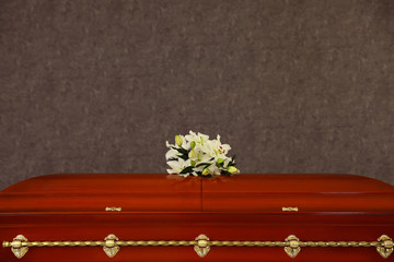 Wooden funeral casket with white lilies at grey wall