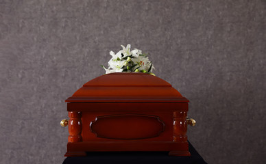 Wooden funeral casket with white lilies at grey wall