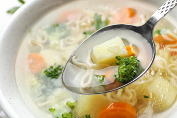 Spoon of fresh homemade vegetable soup over full bowl, closeup