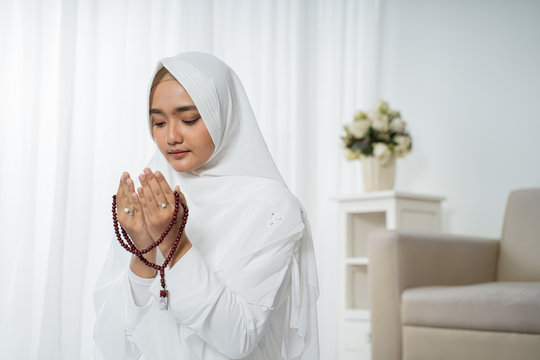 asian young woman praying with Al-Qur'an and prayer beads in white traditional clothes