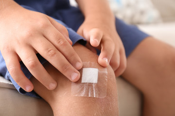 Little boy with adhesive bandage on knee indoors, closeup