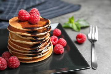 Delicious pancakes with fresh raspberries and chocolate syrup on grey table