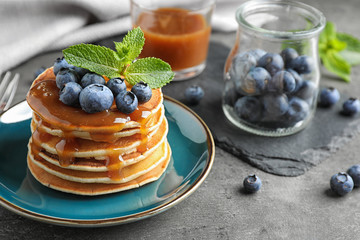 Delicious pancakes with fresh blueberries and syrup on grey table