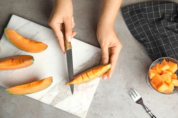 Young woman cutting cantaloupe melon slice at table, top view