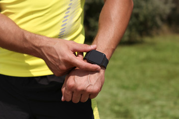 Young man checking pulse with smartwatch after training in park, closeup. Space for text