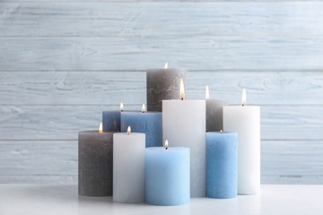 Set of burning candles on table against light wooden background