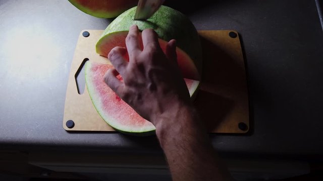 Slicing watermelon an a cutting board in a dark light contrast top down view, with white male model.