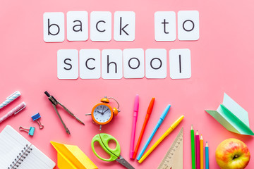 Back to school with stationary, notebook and alarm clock on pink student desk background top view