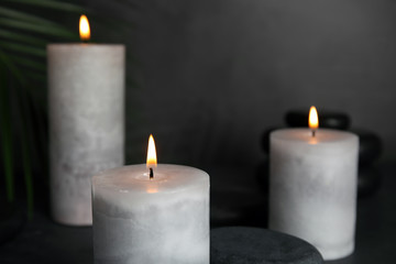 Fototapeta na wymiar Burning candles, spa stones and palm leaf on grey background