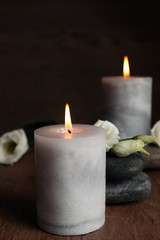 Fototapeta na wymiar Burning candles, spa stones and flowers on wooden table, space for text