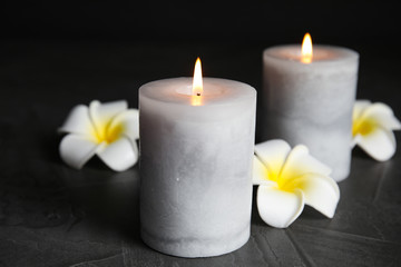 Fototapeta na wymiar Burning candles and plumeria flowers on dark grey table