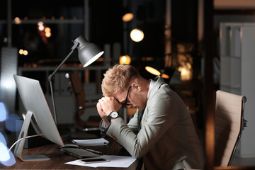Tired young businessman working in office alone at night