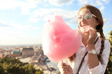 Young woman with cotton candy outdoors on sunny day. Space for text