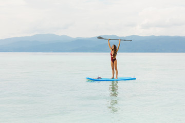 Happy woman standing on sup board and holding paddle. Tropical travel and water activity concept....