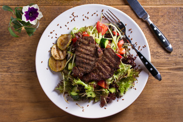 Beef salad: grilled beef steaks with tomatoes, cucumbers, zucchini, lettuce and cabbage, sprinkled with flax seeds. View from above, top studio shot