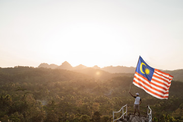 portrait of man on top of the hill in the morning rising malaysia flag celebrating independence day