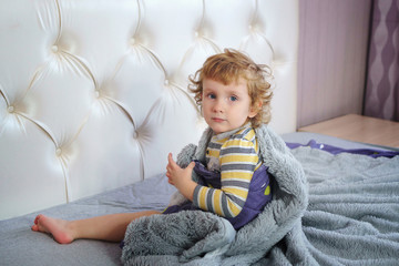 Portrait of a charming baby with golden hair and clear blue eyes. Angel face. Boy sits on the...