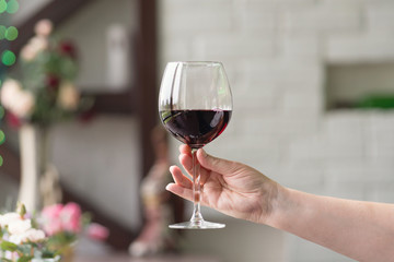 Female hand holding glass with wine on blurred natural background. Space for text. Wine tasting, restaurant, wine tour. Concept alcoholic drinks. 