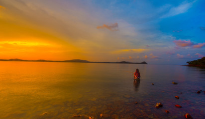 Women are fishing on the coast, Beautiful Sunset in the sky with sky blue and orange light of the sun through the clouds in the sky, Orange and red dramatic colors over the sea. - Image