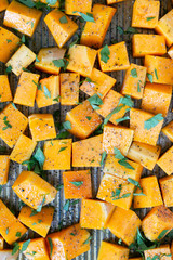 Cubed Butternut Squash on Sheet Pan covered in olive oil, pepper, salt, and parsley, raw vegetable in baking sheet