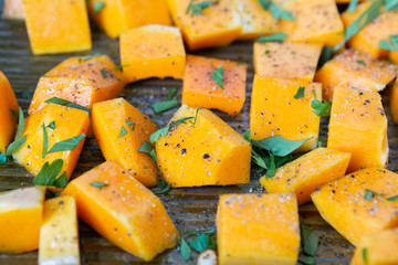 Cubed Butternut Squash on Sheet Pan covered in olive oil, pepper, salt, and parsley, raw vegetable in baking sheet