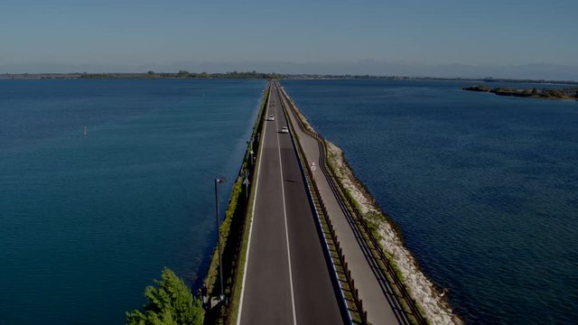 Aerial drone shot of a long road surrounded by large bodies of water in Grado Italy
