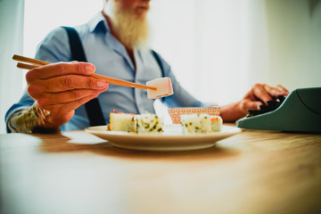 Man enjoying eating fresh colorful asian sushi using chopsticks. This man writing with the old typewriter in the office. Image