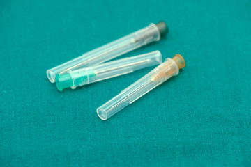 Obraz premium Three color of injection needle with cover isolated on surgical green drape