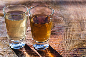 Two shot glasses of Brazilian gold and white cachaca isolated on rustic wooden background. Typical drink from brazil.