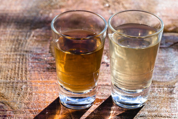 Two shot glasses of Brazilian gold and white cachaca isolated on rustic wooden background. Typical drink from brazil.