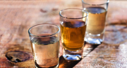 three shot glasses of Brazilian gold and white cachaca isolated on rustic wooden background....