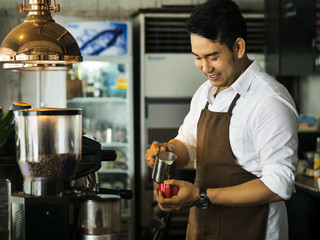 Happy Asian barista pouring milk into red coffee cup for latte art.
