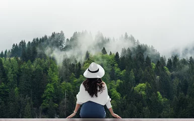 Fotobehang Vrouw met witte hoed die & 39 s ochtends naar een mistig landschap met dennenbossen kijkt © SasinParaksa