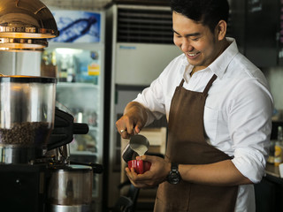 Happy Asian barista pouring milk into red coffee cup for latte art.
