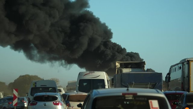 Pillar of black smoke rises into the air ahead of jostling, unsettled traffic jam of cars, trucks and minibus taxis. Some vehicles leave the road to avoid the mayhem.