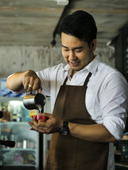 Happy Asian barista pouring milk into red coffee cup for latte art.
