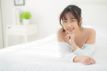 Beautiful portrait young asian woman lying and smile while wake up with sunrise at morning, beauty cute girl happy and cheerful resting on bed in the bedroom, lifestyle and relax concept.
