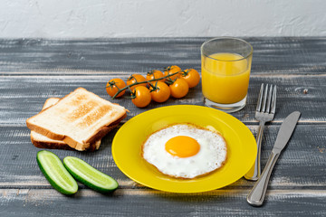 fried egg on yellow plate with cherry tomatoes, cucumbers, orange juice and toast. Delicious nutritious breakfast.