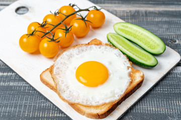 fried egg on toast with cucumbers and cherry tomatoes on white cutting board. Light breakfast