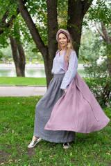 Fototapeta premium young white girl, natural appearance, long hair, beautiful face, gray long skirt, blue shirt, crimson color jacket. Cool to pose on lawn in city park. linen look womens clothing.