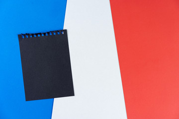 Blacklist France. Mourning, ban, sanctions, politics. black sheet from notebook lies on French flag. Mock up, copy space, pattern, cardboard texture.
