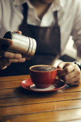 Asian barista sprinkles chocolate powder on drink in red cup.