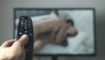 Hand holding TV remote controller. Watching porn
