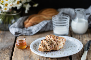 Fresh bread and croissant with milk and honey on a wooden table. Bouquet of daisies. rustic